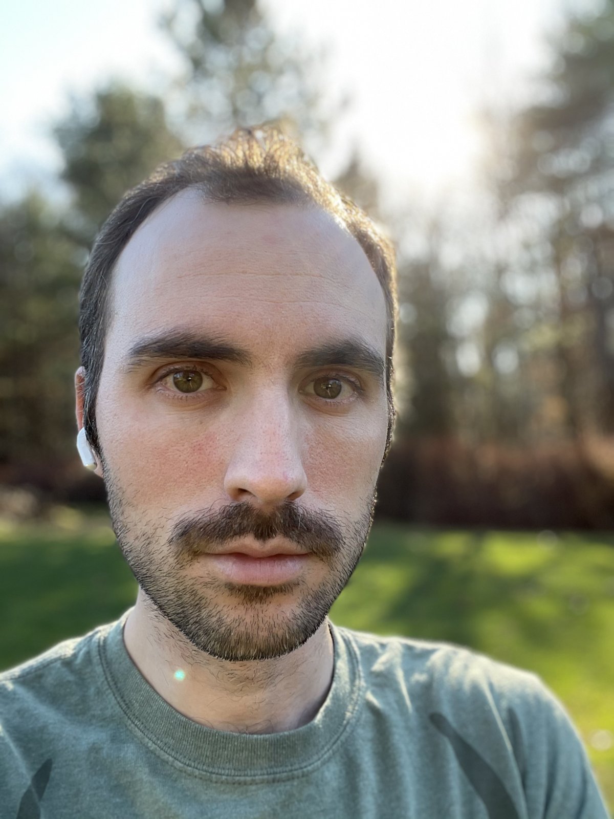 Portrait of Luke Grecki outdoors, trees and a sunlit lawn behind him